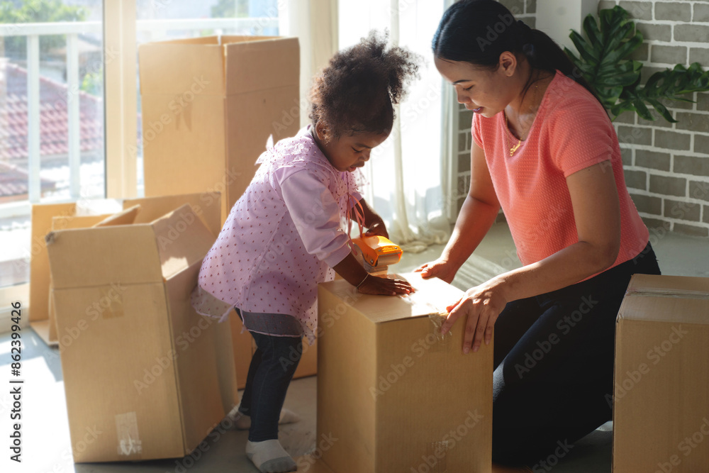 Mother teaches African daughter to stick tape on cardboard boxes at home, sticking adhesive tape on cardboard box Mother teaches African daughter to stick tape on cardboard boxes at home, sticking adhesive tape on cardboard box
