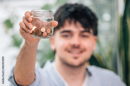 Fotografia pot with savings or coins close-up in hand of happy young man