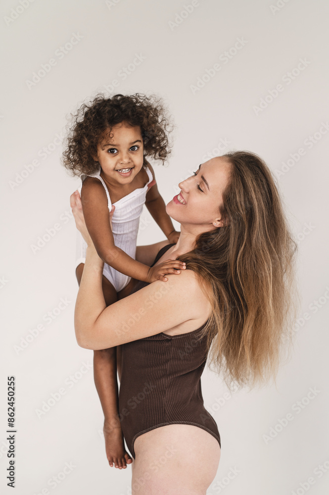 Interracial family having fun on white background. Mixed marriages concept. European mother and 2 years mulatto black african daughter hugs, kiss and laughth on cozy white plaid Interracial family having fun on white background. Mixed marriages concept. European mother and 2 years mulatto black african daughter hugs, kiss and laughth on cozy white plaid