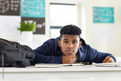 Obraz na plátně In school, African American teenage boy resting head on desk, looking thoughtful