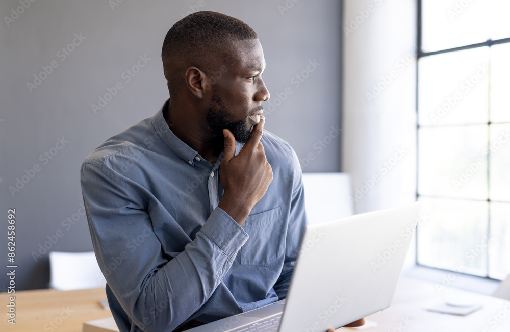 Holding laptop, business man looking out window, contemplating ideas in office Holding laptop, business man looking out window, contemplating ideas in office