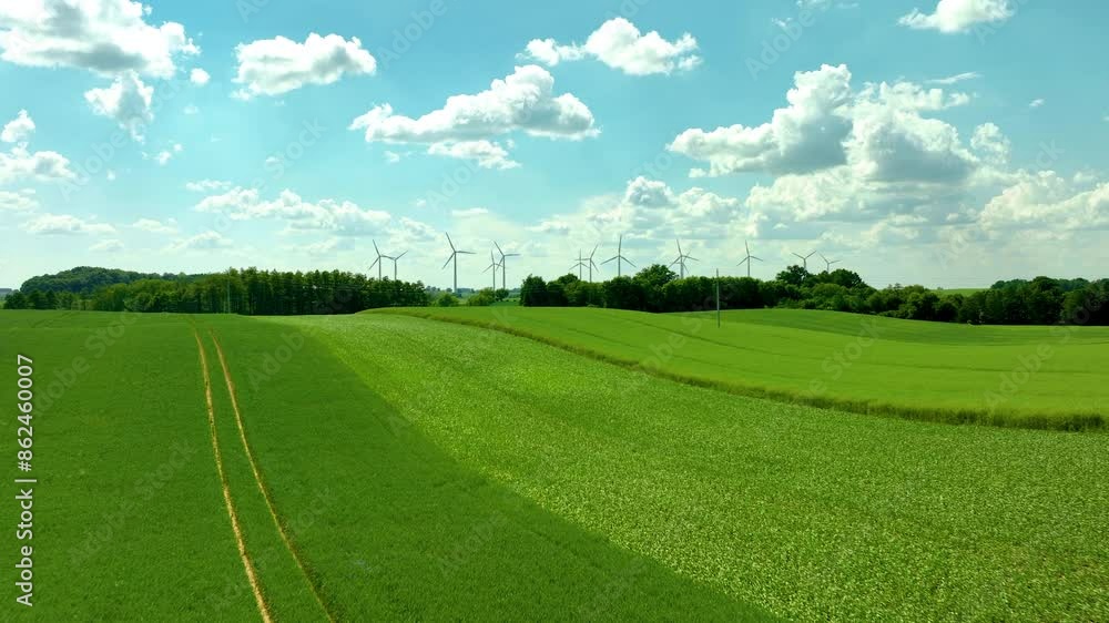 Aerial shot of green fields with wind turbines, bright blue sky, and scattered clouds - forward Aerial shot of green fields with wind turbines, bright blue sky, and scattered clouds - forward