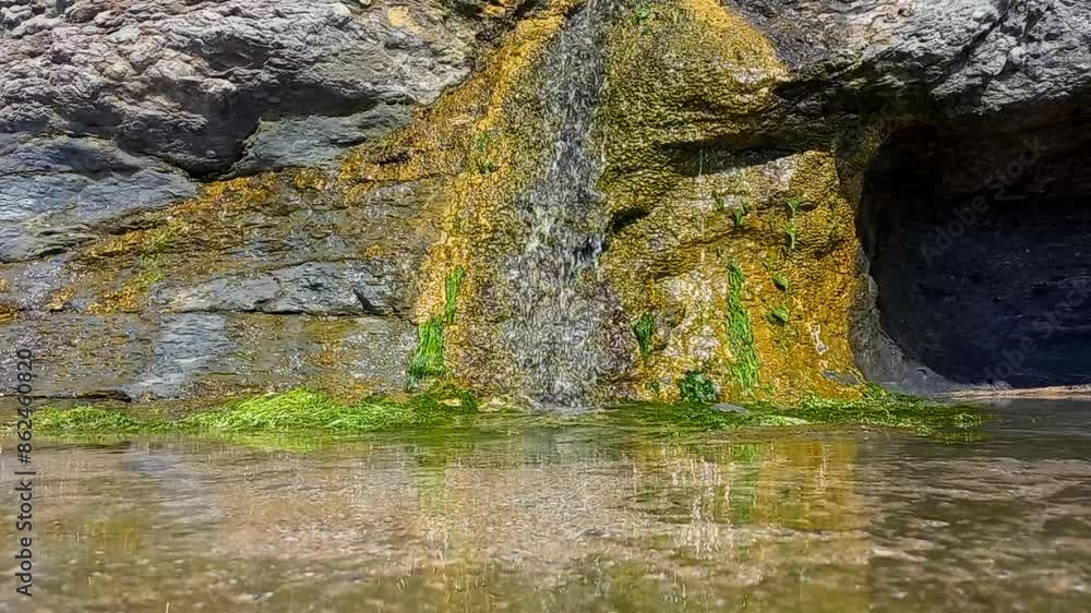 Water running down the rocks in sea caves near the coast, forming a mirror of water and green slime on the rocks Water running down the rocks in sea caves near the coast, forming a mirror of water and green slime on the rocks