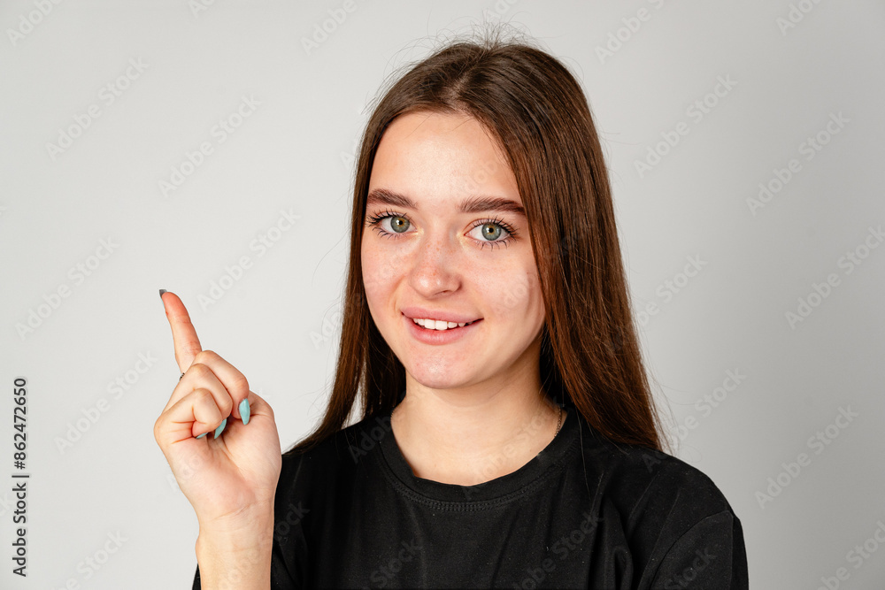 Smiling Young Woman Pointing to Copy Space Against a Grey Background Smiling Young Woman Pointing to Copy Space Against a Grey Background