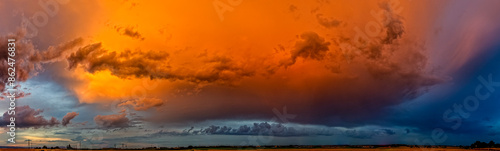 Panoramafoto einer abziehenden Gewitterwolke, die vom Licht der untergehenden Sonne orange angestrahlt wird photo