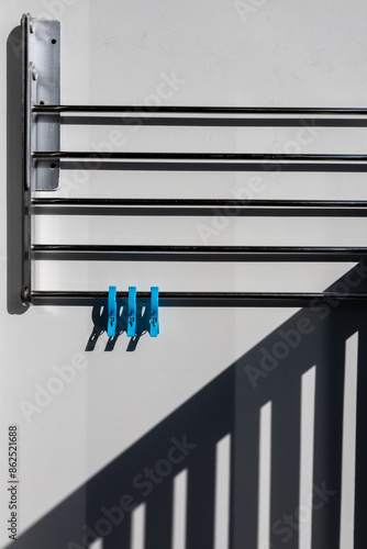 Wallpaper Mural Three.  Three blue pegs on a metal drying rack against a white wall in bright sunshine with strong shadows. Torontodigital.ca
