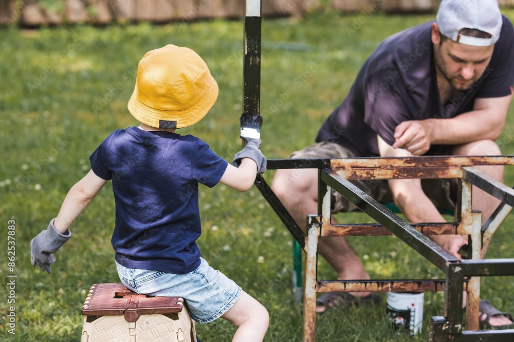 Father and son work with a brush and apply black paint to the rust. People paint metal structures. Rust removal. Teaching a child to work. Father and son work with a brush and apply black paint to the rust. People paint metal structures. Rust removal. Teaching a child to work.