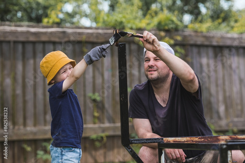 Father and son work with a brush and apply black paint to the rust. People paint metal structures. Rust removal. Teaching a child to work. photo