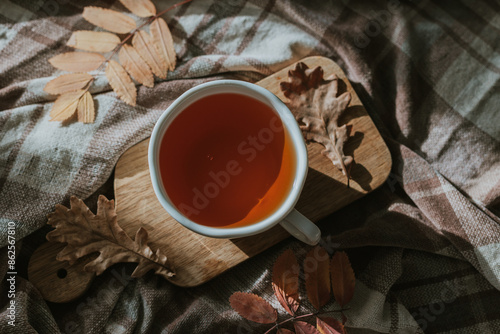 Wooden tray with hot tea and autumn fall leaves on cozy blanket on bed. Cozy home atmosphere