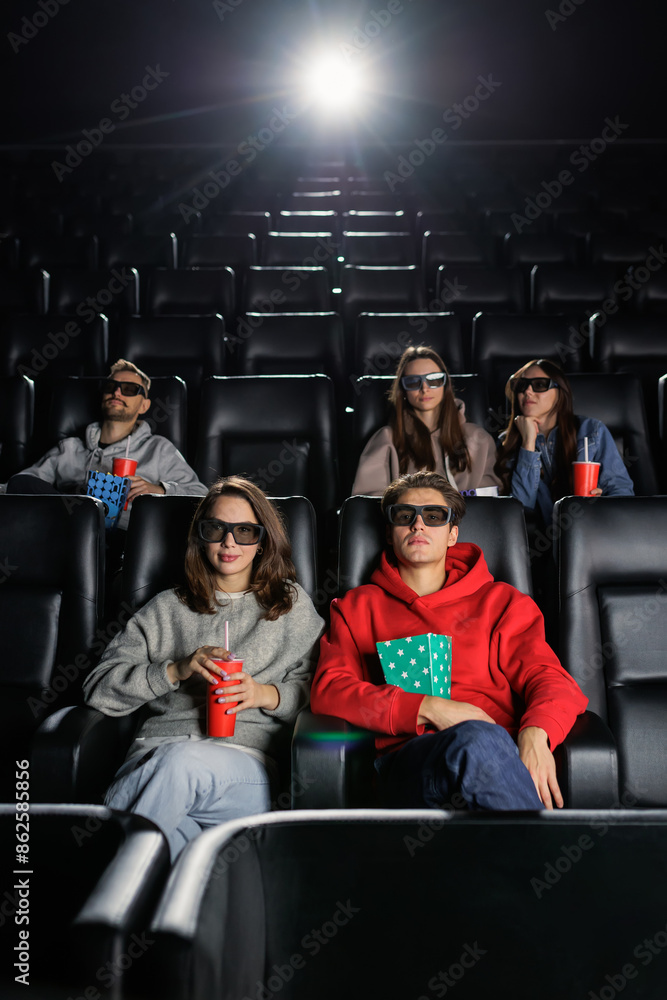 Obraz premium Vertical photo of people in the cinema. A young couple eats popcorn and watches a movie