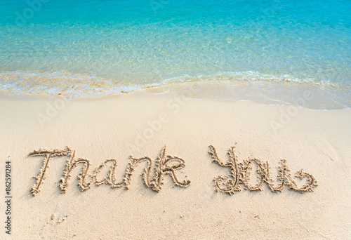 Thank you lettering on the beach with wave and clear blue sea. Thank you card with message written in golden sand on clean beach background. Gratitude concept. Copy space.