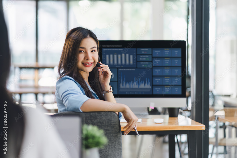 Fototapeta premium Operator wearing a headset, using a dashboard on laptop for data analysis in modern office.