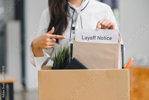 Employee packing personal belongings into cardboard box after receiving layoff notice in modern office.