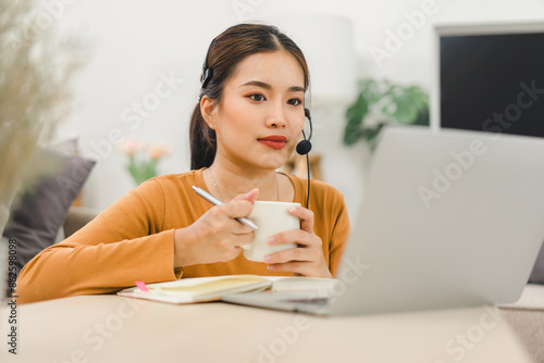 Woman wearing a headset, actively engaged in an online learning session with a teacher displayed on a computer screen, studying from home.