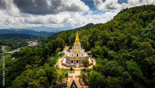 Aerial view of Phrathat Chedi Srinagarindra Stit Maha Santi Khiri Temple and Pagoda surrounded by forested mountains under a cloudy sky, Mae Salong Nok, Chiang Rai District, Thailand. photo
