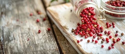 Pink peppercorn spilled from a glass jar onto a white wooden cutting board, captured in a close-up image on a vintage wooden table with copy space. photo