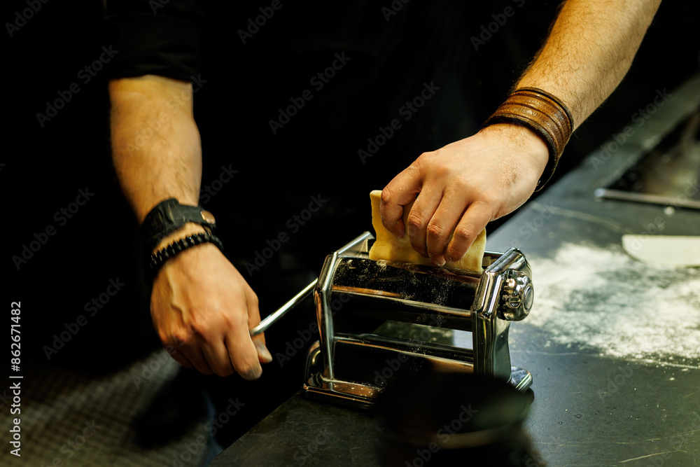 Close-up of hands using a traditional pasta maker to flatten dough on a kitchen counter Close-up of hands using a traditional pasta maker to flatten dough on a kitchen counter