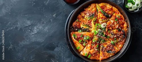 Delicious Korean pancake with spring onions, kimchi, and other vegetables served in a sizzling pan with a spicy dipping sauce, presented on a copy space image. photo
