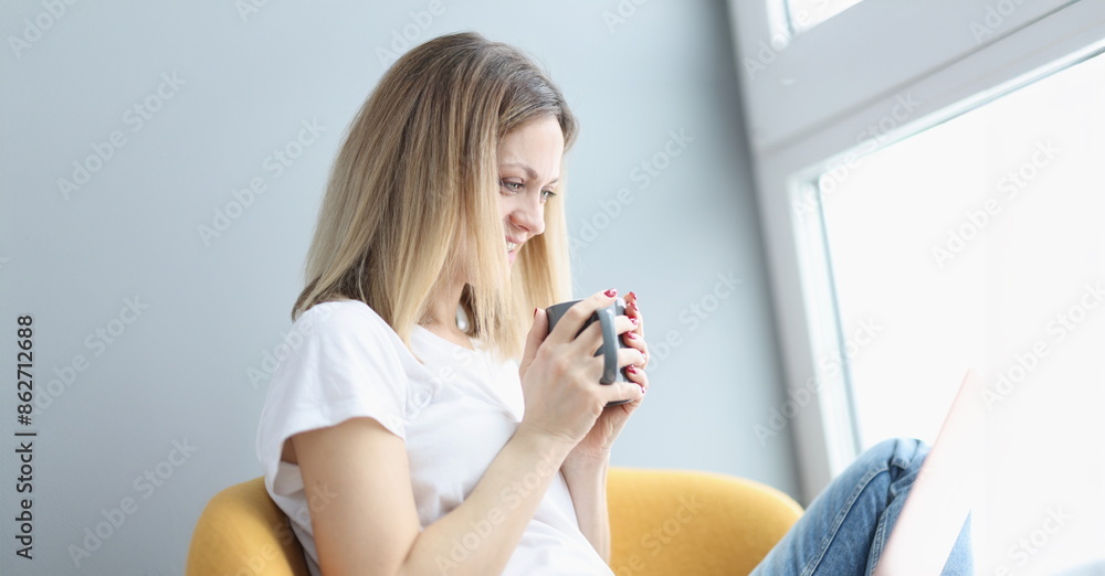 Woman sitting in chair with laptop and drinking tea. Remote work online concept Woman sitting in chair with laptop and drinking tea. Remote work online concept