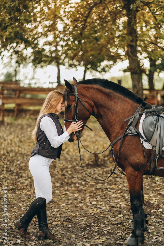 Fototapeta premium A young female equestrian stands near her horse and prepares for a competition.