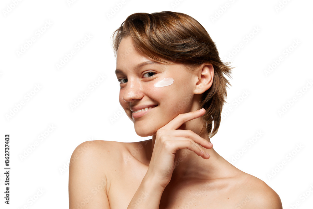 Woman with short brown hair smiles applying lotion to her cheek against white studio background. Morning routine. Concept of youth, beauty and fashion, cosmetic product, dermatology. Ad Woman with short brown hair smiles applying lotion to her cheek against white studio background. Morning routine. Concept of youth, beauty and fashion, cosmetic product, dermatology. Ad