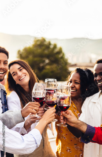 Bild auf Leinwand Vertical photo of happy group of young friends celebrating together cheering with red wine glasses at terrace summer party during sunset