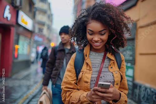A smiling young woman checks her phone while walking on a wet and rainy city street, depicting the blend of technology and daily life in a lively urban environment.