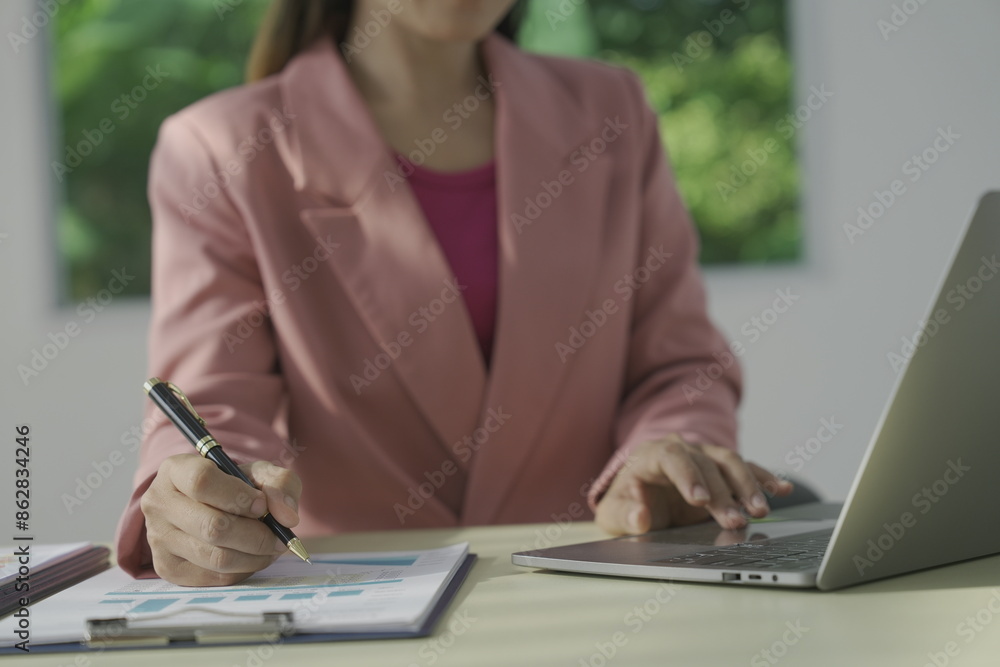 Happy young businesswoman in bright colored shirt uses computer and laptop in modern office Smiling manager while working on finance and marketing project Drink tea or coffee from a glass Happy young businesswoman in bright colored shirt uses computer and laptop in modern office Smiling manager while working on finance and marketing project Drink tea or coffee from a glass