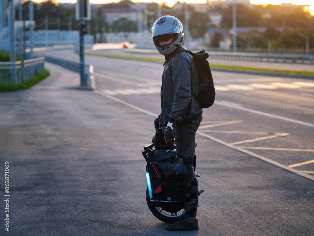 Obraz premium A man rides on an EUC electric wheel. He is equipped with a helmet, gloves and knee pads for safe movement around the city. Urban electric transport
