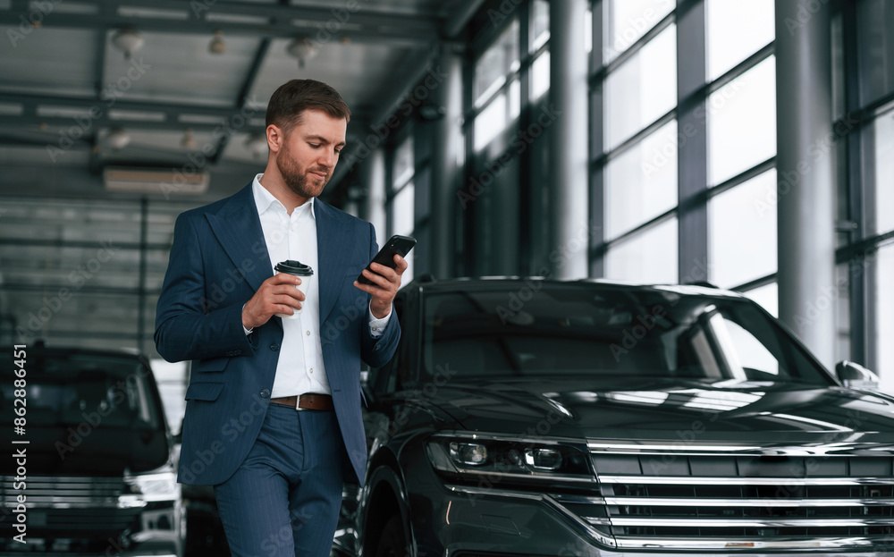 Break, with coffee and smartphone. A businessman is in a car dealership Break, with coffee and smartphone. A businessman is in a car dealership