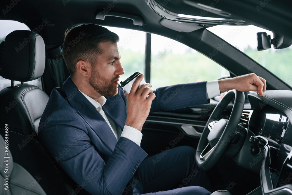 Driving and drinking coffee. Businessman is in the brand new car Driving and drinking coffee. Businessman is in the brand new car