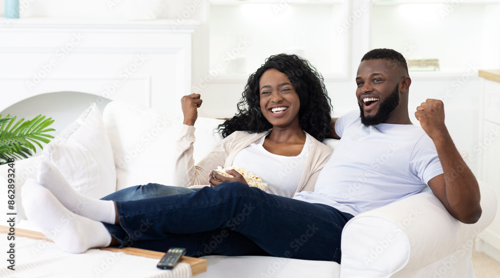 A couple celebrates their teams victory while watching television on a white couch in their home. A couple celebrates their teams victory while watching television on a white couch in their home.
