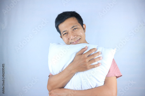 comfortable facial expression of asian young man hug a pillow, isolated on white background photo