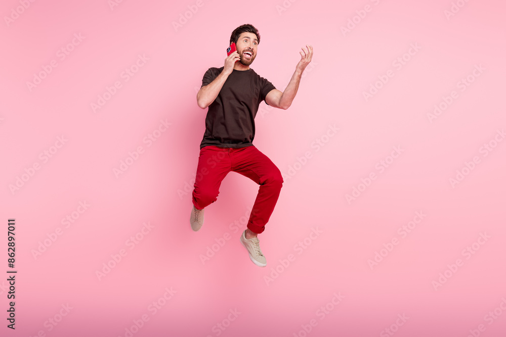 Full size photo of positive funny man wear brown t-shirt talk on smartphone jumping look empty space isolated on pink color background Full size photo of positive funny man wear brown t-shirt talk on smartphone jumping look empty space isolated on pink color background