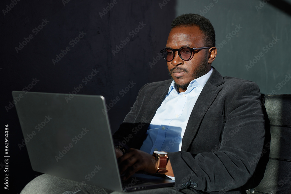 Portrait Of Pensive African Business Man In Glasses Sitting At Desk With Laptop In Home Office Portrait Of Pensive African Business Man In Glasses Sitting At Desk With Laptop In Home Office