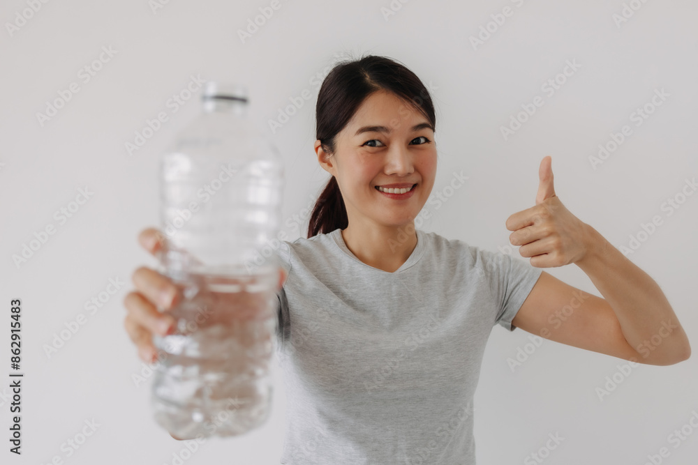 Asian Thai woman smiling and holding bottle of mineral water, showing good point, standing isolated over white background wall. Asian Thai woman smiling and holding bottle of mineral water, showing good point, standing isolated over white background wall.