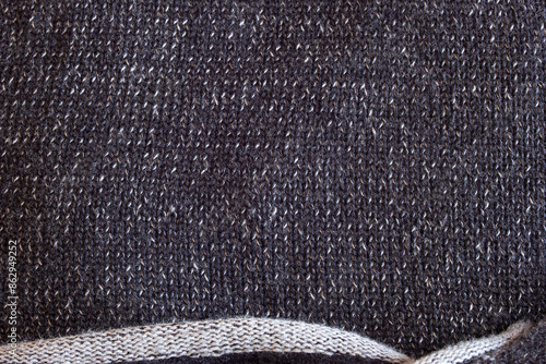 Close up of a sweater with  white and dark gray threads creates a monochromatic depth. The bottom edge, with its sparse weave and raw finish.