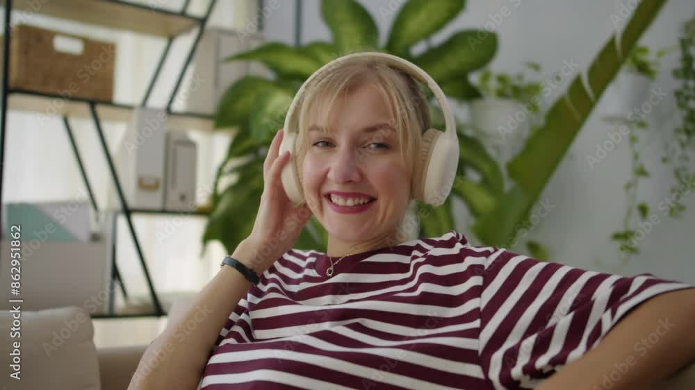 Medium portrait of smiling Caucasian woman smiling at camera while listening to music in headset indoors Medium portrait of smiling Caucasian woman smiling at camera while listening to music in headset indoors