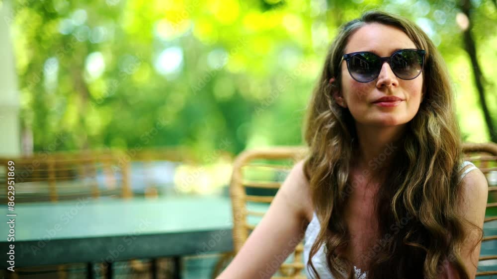 Woman wearing sunglasses looking around at a table surrounded by trees Woman wearing sunglasses looking around at a table surrounded by trees