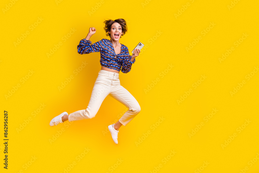 Full body photo of young successful brown bob haired jumping raised fist up winning in online casino isolated on yellow color background Full body photo of young successful brown bob haired jumping raised fist up winning in online casino isolated on yellow color background