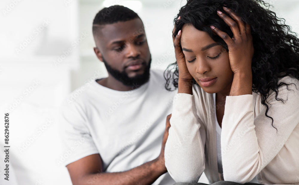 Obraz premium A man sits beside a woman who is upset and has her head in her hands. They are both indoors.