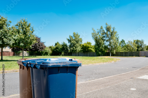 Blue and brown residential collection wheelie bins ready to be collected from a UK housing estate. A green space area is seen in the background. photo