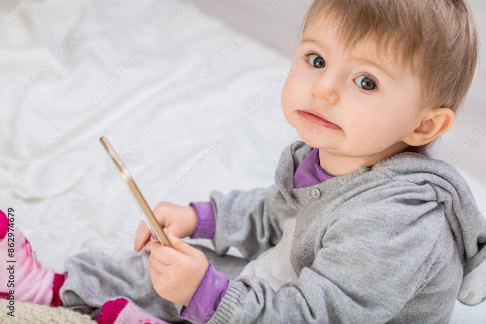 Baby girl holding smartphone with guilty expression Baby girl holding smartphone with guilty expression