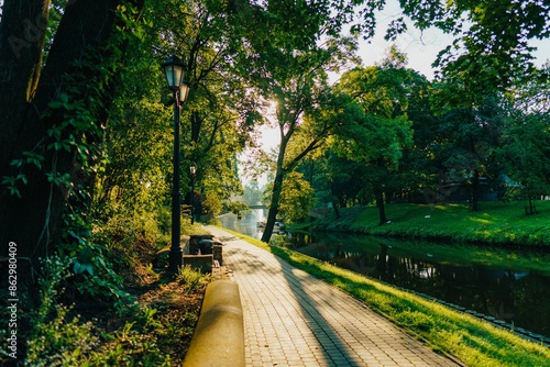 Fototapeta Naklejka Na Ścianę i Meble -  Scenic view of a park pathway alongside a tranquil river in Riga, Latvia