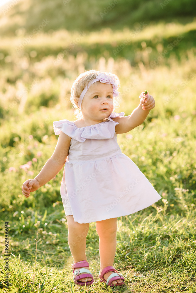Child running in mountains on a summer day. Kid playing in spring sunlight outdoors. Toddler walks on green grass in field at sunset. Happy childhood. Beautiful cute girl walking in nature. Closeup. Child running in mountains on a summer day. Kid playing in spring sunlight outdoors. Toddler walks on green grass in field at sunset. Happy childhood. Beautiful cute girl walking in nature. Closeup.