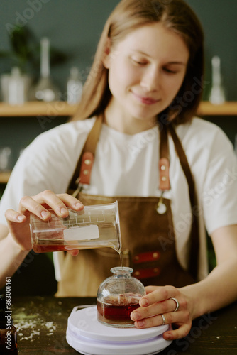 Young perfumer pouring back tea shade liquid into round glass flask, she enjoying process