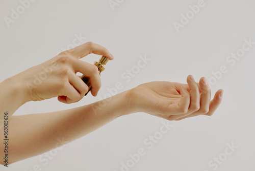 Female manicured hands holding brown glass flask full of new aroma and spraying it on her wrist