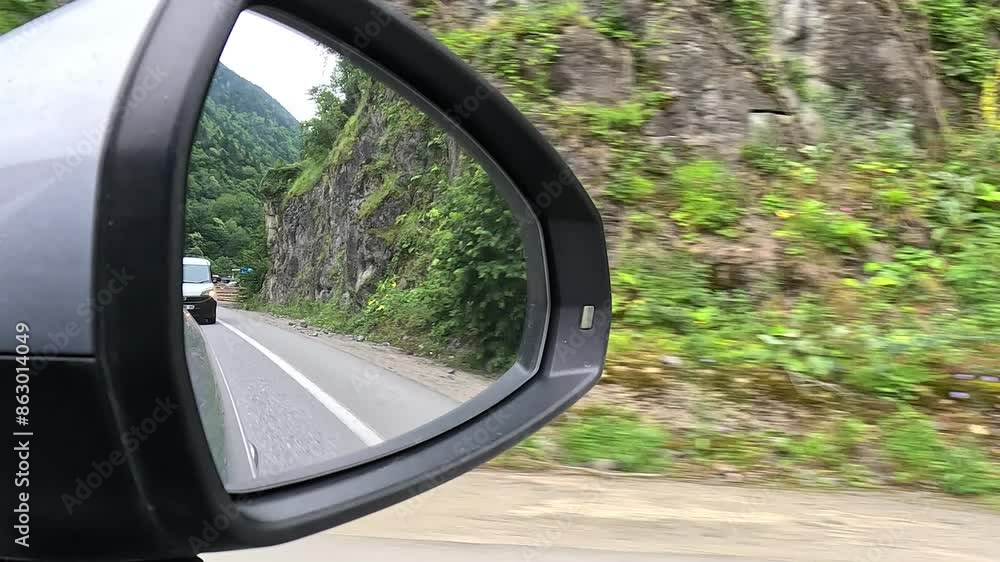 Red automobile in motion. View in the rear view side mirror of a auto, driving a red car along the track Red automobile in motion. View in the rear view side mirror of a auto, driving a red car along the track