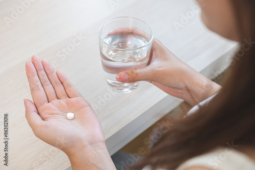 Quadro em tela Sick asian young woman, girl holding tablet pill on hand, painkiller medicine from fever, stomach pain, headache for treatment, take drug or vitamin with glass of water at home