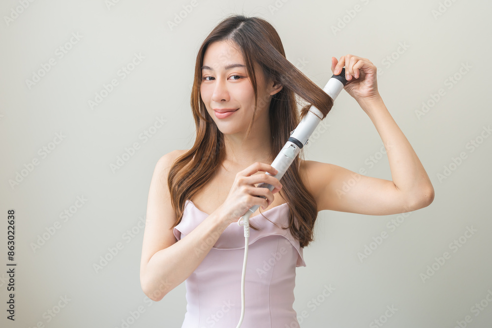 Beautiful curly brunette, attractive asian young woman, girl smiling using curler, curling iron long hair with ceramic curler straightener at home. Hairstyle and Hairdressing. Beauty and hair care. Beautiful curly brunette, attractive asian young woman, girl smiling using curler, curling iron long hair with ceramic curler straightener at home. Hairstyle and Hairdressing. Beauty and hair care.